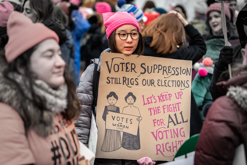 Image of woman holding placard "Voter suppression still rigs our elections. Let's keep up the fight for ALL voting rights" and an image of two women holding a "votes for women" placard.